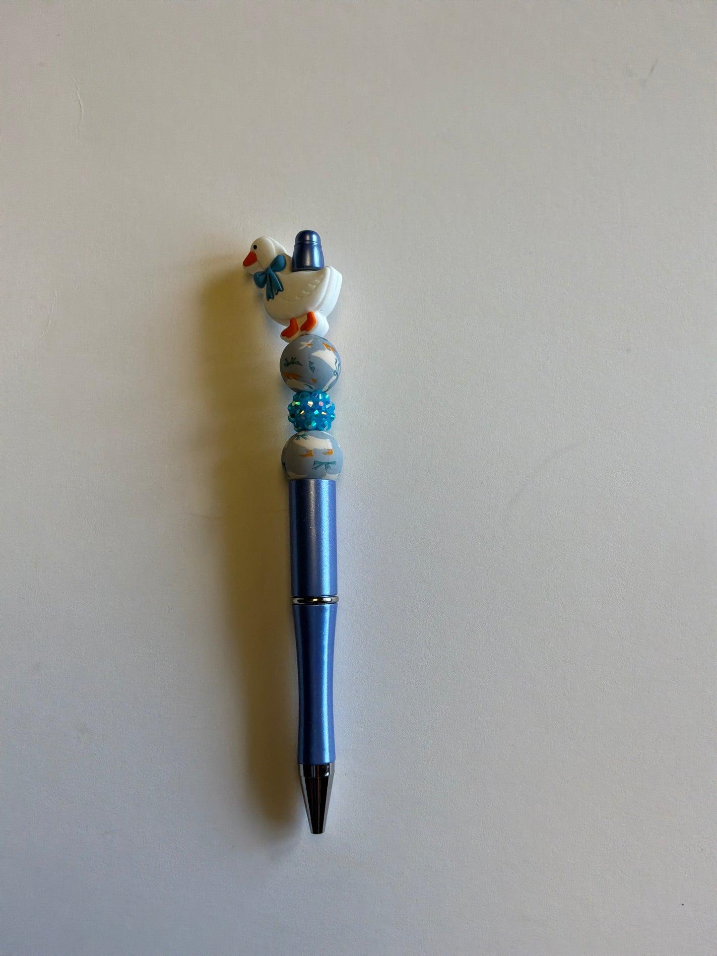 Beaded goose with blue bow on a metallic periwinkle pen